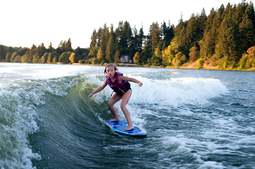 Young female wake surfing behind a ski boat and wearing a lifejacket