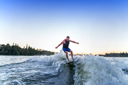 Adult male wake surfing behind a ski boat on a local reservior