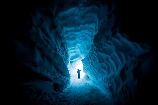 Male carrying skis on shoulders, walking out from glacier cave.