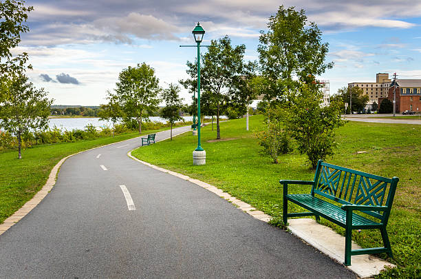 Riverside Paved Path and Cloudy Sky Winding Riverside Path Lined with Benches and Trees new brunswick canada photos stock pictures, royalty-free photos & images
