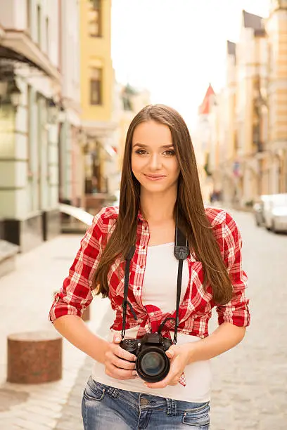 Pretty young girl holding camera and standing on the street