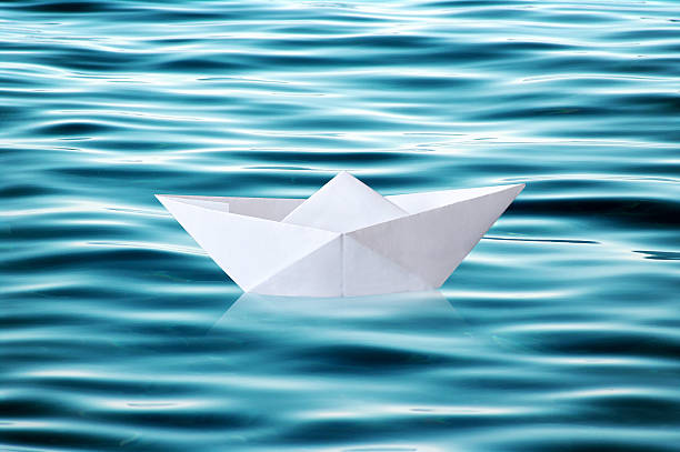 istock Paper boat floating on rippled water 614500108