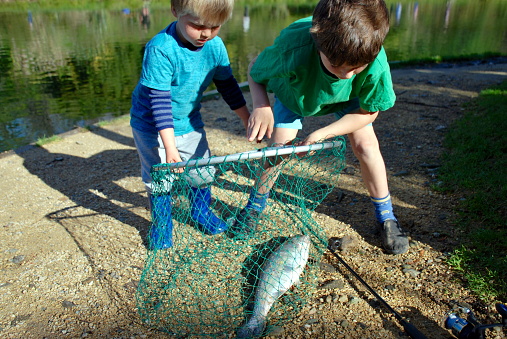 Brothers fishing by a river on an Autumn day. A big brother helps his younger sibling with the caught fish.