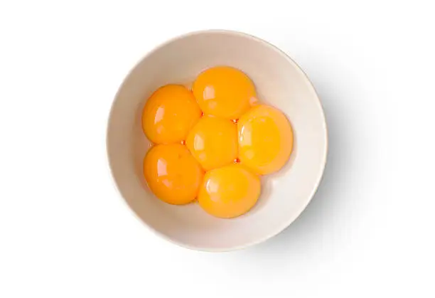 Six fresh and shiny yolks in a bowl on white background.