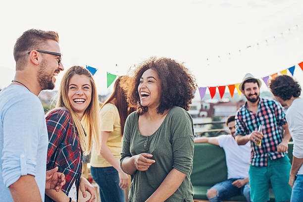 Rooftop celebration Group of young people chatting and laughing on a rooftop party. friends laughing stock pictures, royalty-free photos & images