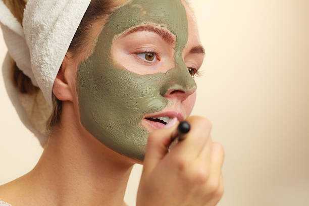 istock Woman applying with brush clay mud mask to her face 614509702