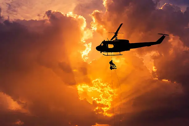 silhouette soldiers in action rappelling climb down from helicopter with military mission counter terrorism assault training on sunset background 