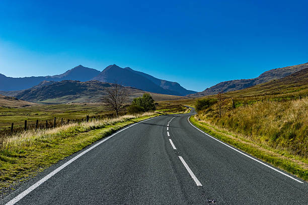 Winding Mountain Road A winding mountain road in Snowdonia National Park, Wales, UK. Mountain range in the background with the empty road winding into the distance on a clear, sunny, summers day.  gwynedd photos stock pictures, royalty-free photos & images