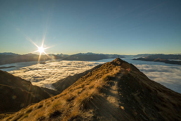 istock Distant woman stands on mountain summit above clouds 614609794