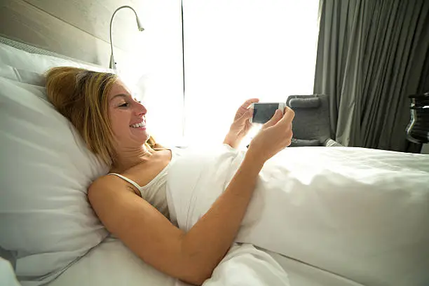 Photo of Young woman in bed checking mobile phone