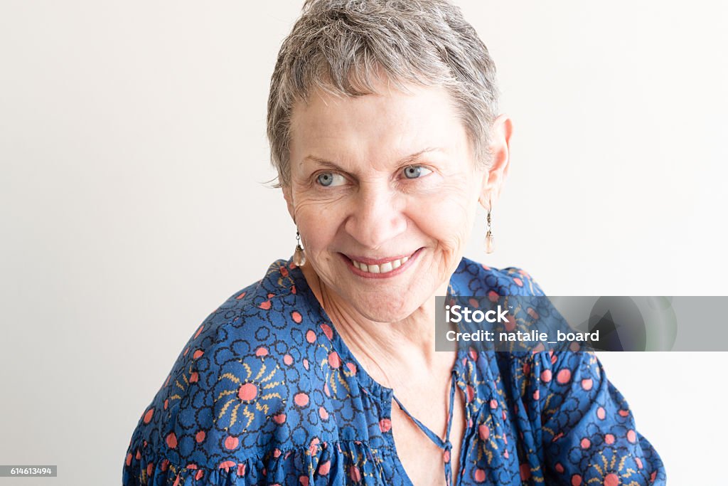 Older woman laughing Older woman with drop earrings and blue top laughing against neutral background 65-69 Years Stock Photo