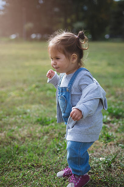 istock baby girl walking in a park on a grass 614617844