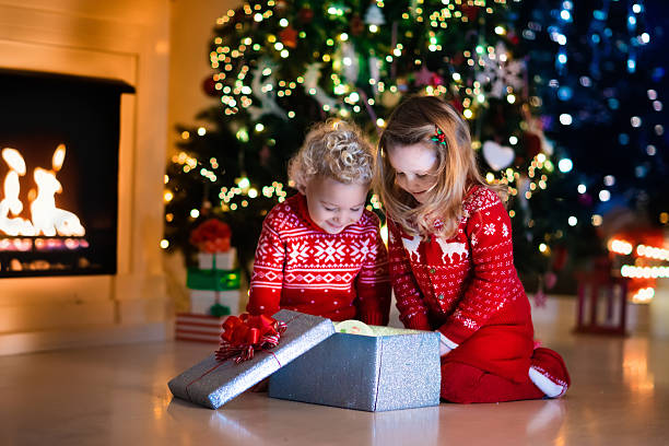 istock Kids opening Christmas presents at fireplace under Christmas tree 614618380