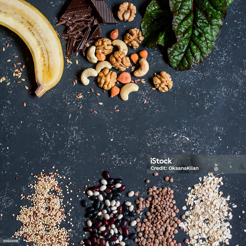 Magnesium rich food -  banana, chocolate, nuts, chard, quinoa, beans Magnesium rich food -  banana, chocolate, walnuts, cashews, chard, quinoa, beans, oatmeal, lentils. On a dark background, top view. Food background Magnesium Stock Photo