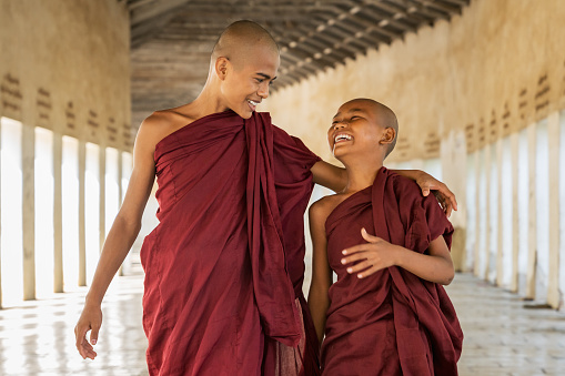 Two happy young Burmese buddhist novice monks in their typical clothing having fun together walking along monastery archway with bright smiles. Bagan, Mandalay Region, Myanmar.