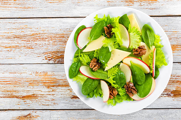 salad of apple, spinach, cheese, lettuce leaves, caramelized wal salad of apple, spinach, cheese, lettuce leaves Frise, caramelized walnuts, cranberry on white dish on peeling paint planks,  view from above green apple slice overhead stock pictures, royalty-free photos & images