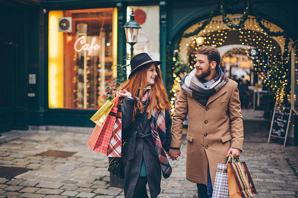 Christmas shopping Young couple walking in front of Christmas store windows. Holding shopping bags. Wearing warm clothing. Vienna, Austria. Smiling and talking. holiday shopping stock pictures, royalty-free photos & images