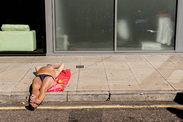London, UK - September 11, 2016: Man wearing speedos lying down on a red beach towel and sunbathing on the pavement of a street in Shoreditch, East London, UK