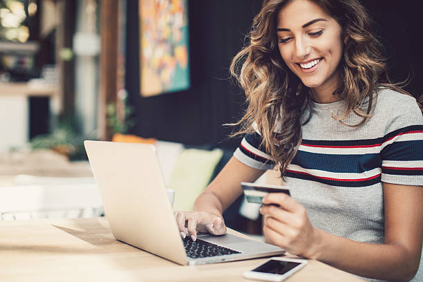E-commerce Smiling young woman holding a credit card and typing on a laptop. financial wellbeing stock pictures, royalty-free photos & images