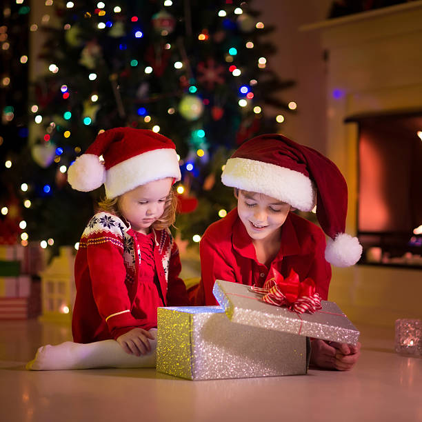 istock Kids opening Christmas presents at fireplace under Christmas tree 614643018