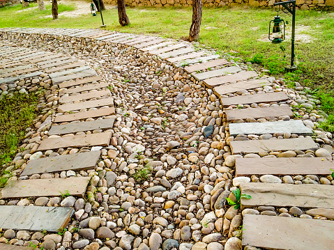 Circular stone pathway on gravel, overgrown with various weeds