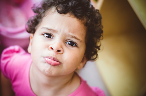 Stock photo of a little girl who is looking up to the camera with her sad face. She is pouting to show her spot under her nose. This file has a signed model release.