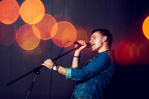 Young Man Singing with Microphone. Singer Performance. Concert and Music Concept. Toned Photo with Bokeh.