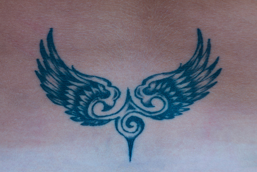 The tattoo in the shape of wings on the back. Simple tattoo for female body decoration.