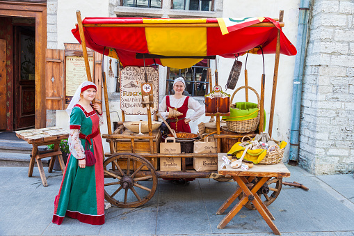 Tallinn, Estonia - June 2, 2016: Beautiful girls in national medieval dresses are selling nuts on a wooden cart in the Historical Center of Tallinn city. Tallinn, Estonia.
