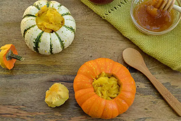 Two baked mini-pumpkins stuffed with spiced pumpkin puree, served with honey, on green dishcloth and wooden table, viewed from above- seasonal food concept