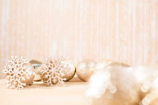 Holiday background.  Shiny gold, beige Christmas ornaments lie on a beige backdrop with snowflakes.  No people in holiday scene.