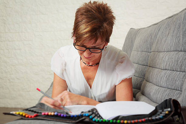 istock Senior woman on couch, drawing in coloring book 614720014