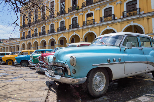 Havana, Сuba - May 28, 2014: American old cars parked in front of a yellow colonial building