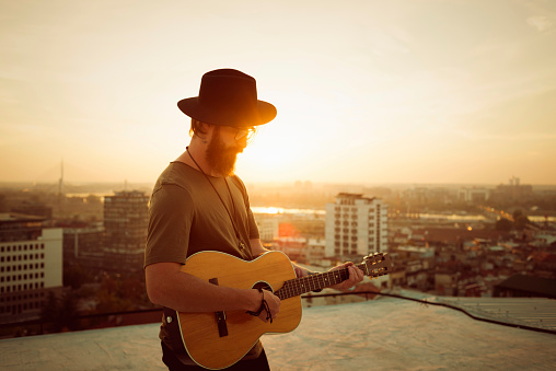 bearded musician playing the guitar on the roof of a building in the city