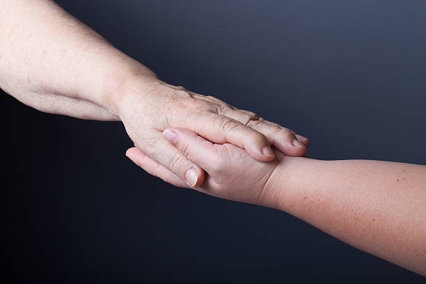 istock Hands of elderly and young women on black background 614723078
