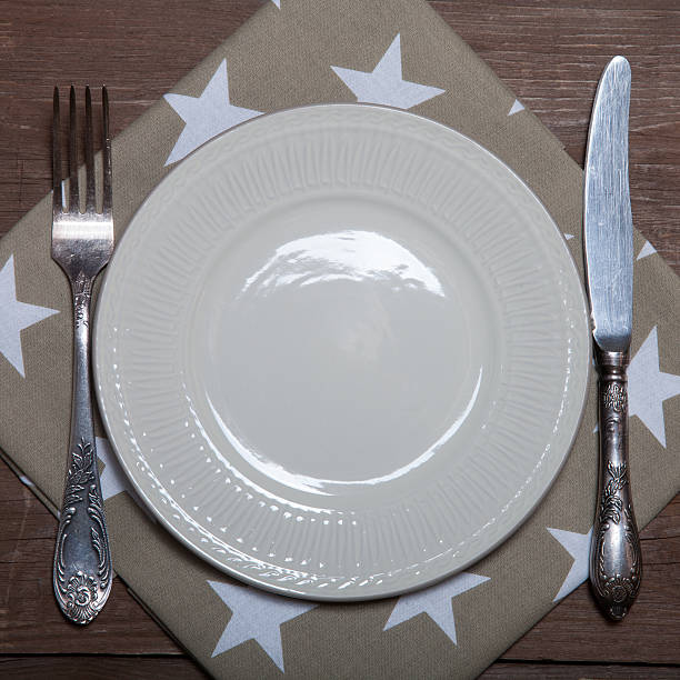 istock Plate, fork and knife on napkin on wooden background 614730264