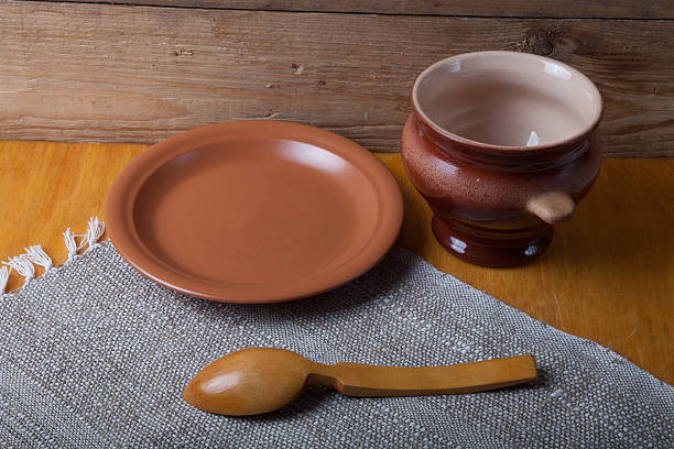 Rustic still life. Clay pot, spoon and plate on linen napkin. Wooden background.