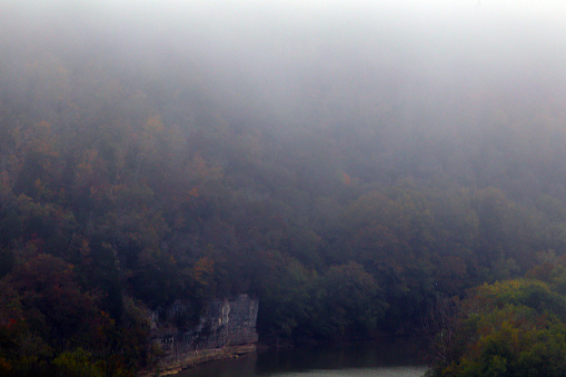 Fog settles in over a river lined by sheer rock and colorful trees of autumn