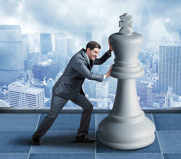 istock Businessman Attempting To Push Chess Piece Against Urban Backdrop 614736528