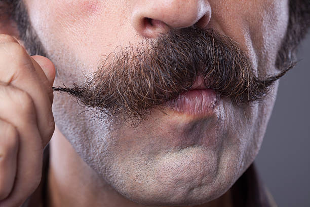 mid adult man curling up his handle bar mustache - mustache imagens e fotografias de stock