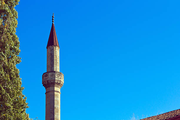 Upper part of the minaret The upper part of the minaret of the mosque against the blue clear sky. Nearby you can see the tree green and part of the roof. Horizontal landscape mullah photos stock pictures, royalty-free photos & images