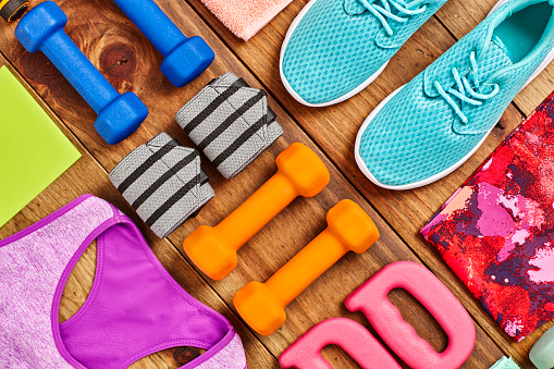 Variety of sports equipment arranged on hardwood floor. Directly above flat lay shot of dumbbells placed with wristbands  handles  towel  shoes and clothing on wood. All are representing healthy lifestyle. Knolling Concept.