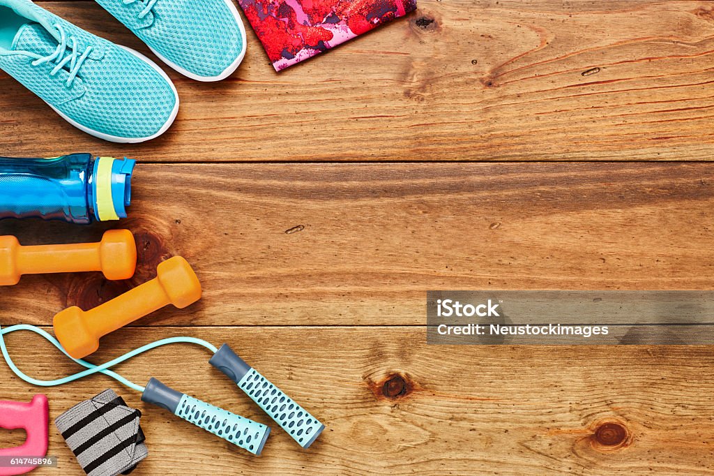 Directly above shot of sports equipment on hardwood floor Directly above flat lay shot of sports equipment on hardwood floor. Sports shoes are placed with water bottle  dumbbells  leggings and jump rope on wood. All are representing healthy lifestyle. Exercise Equipment Stock Photo