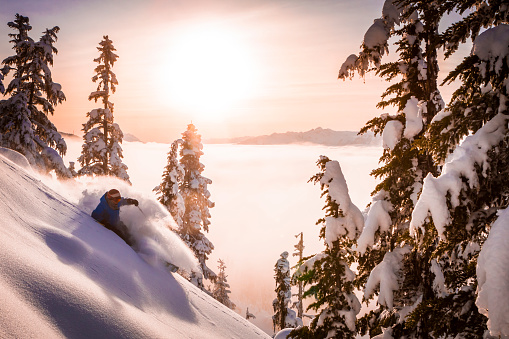 Athletic male skier doing big fresh powder turns in sunset above the clouds.