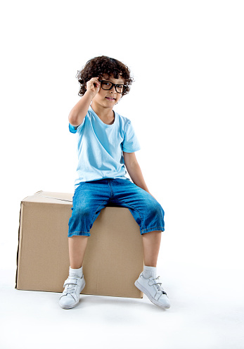 Little boy sitting on a cardboard box against white background.