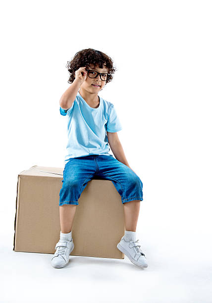 маленький мальчик, сидящий на картонной коробке на белом фоне - glasses child little boys happiness стоковые фото и изображения
