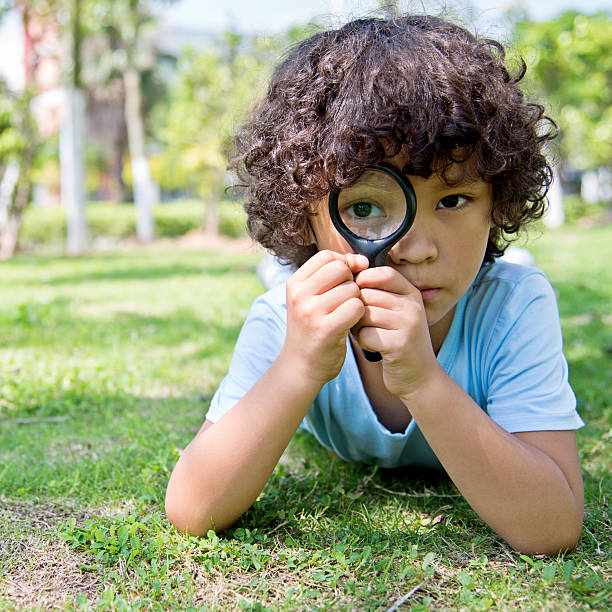 istock Little boy with magnifying glass in park 614833338