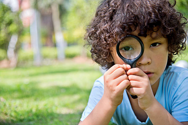 istock Little boy with magnifying glass in park 614833436