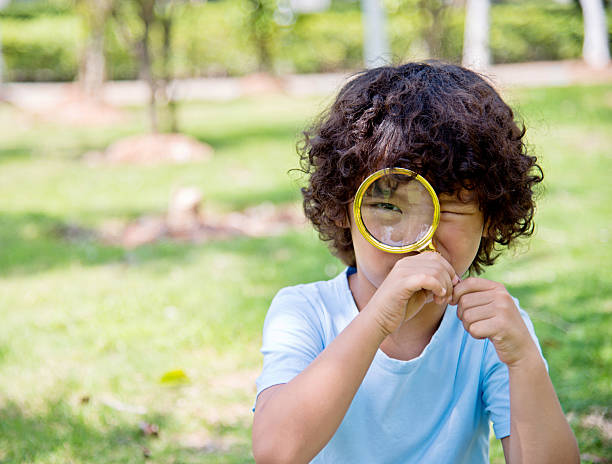 istock Little boy with magnifying glass in park 614833840