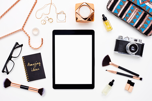 Flat lay of digital tablet surrounded with gold beauty products